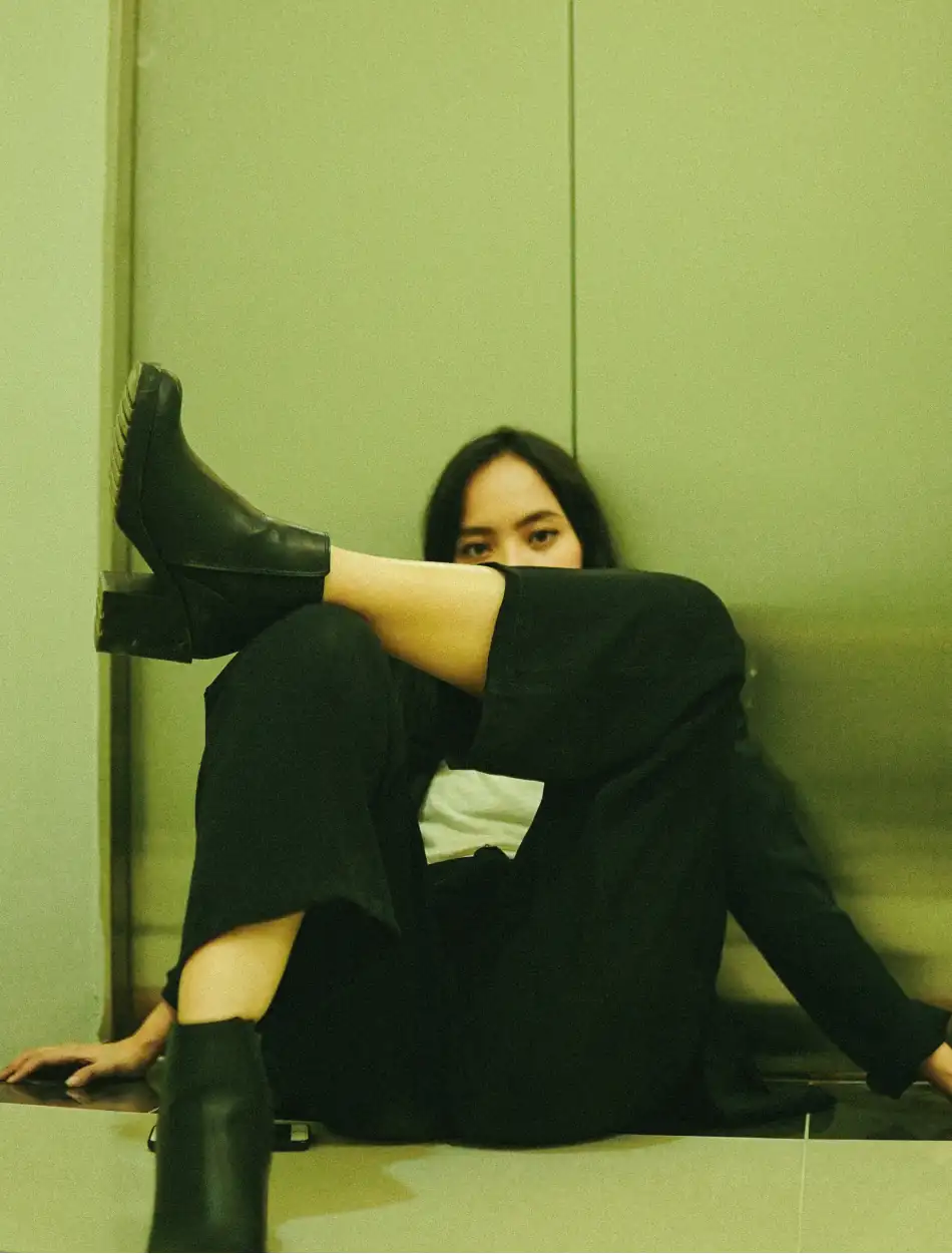 Woman sitting against an elevator door, with her leg up to her knee