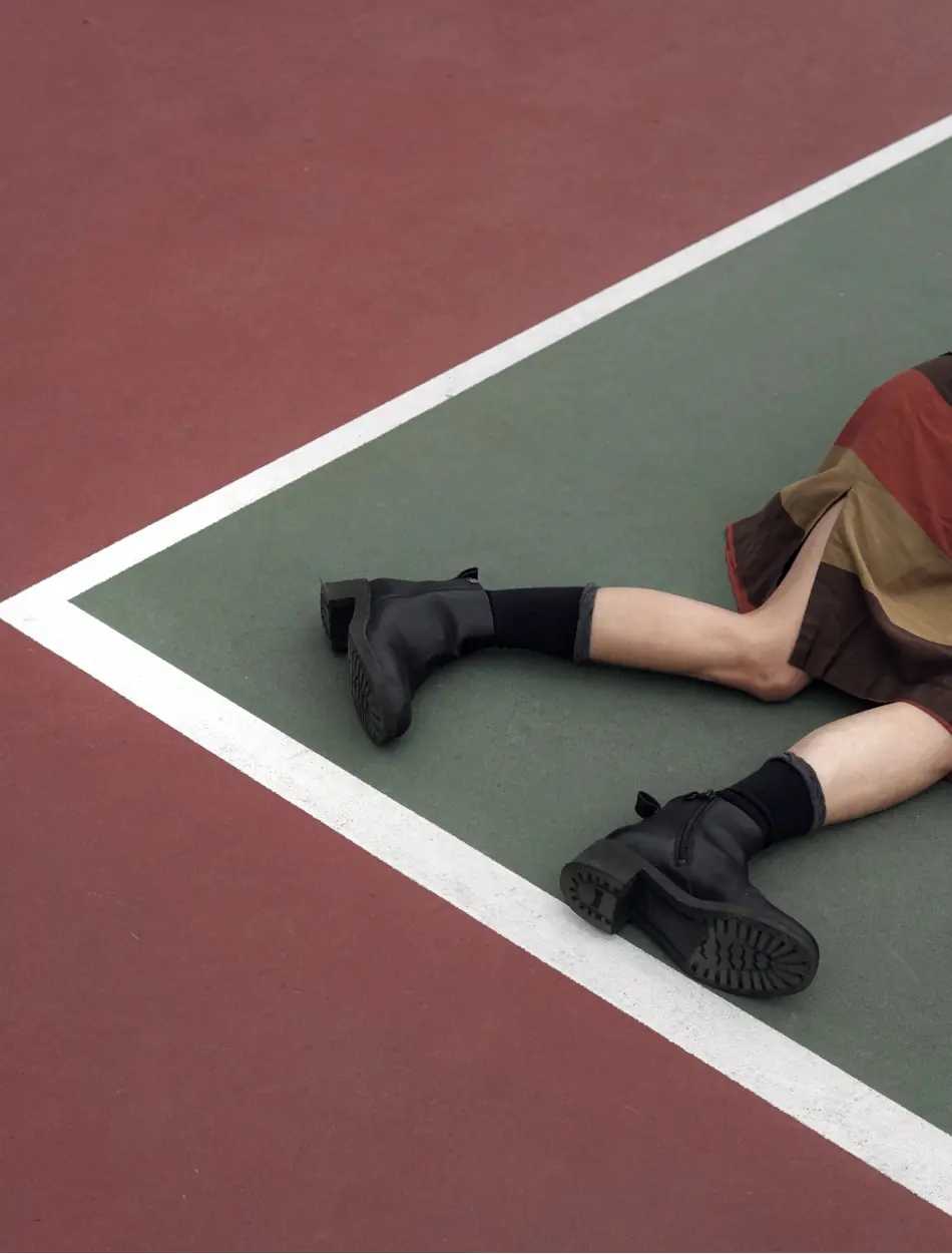 A close up a the boots of a woman lying on a green and red tennis field, super retro vibe
