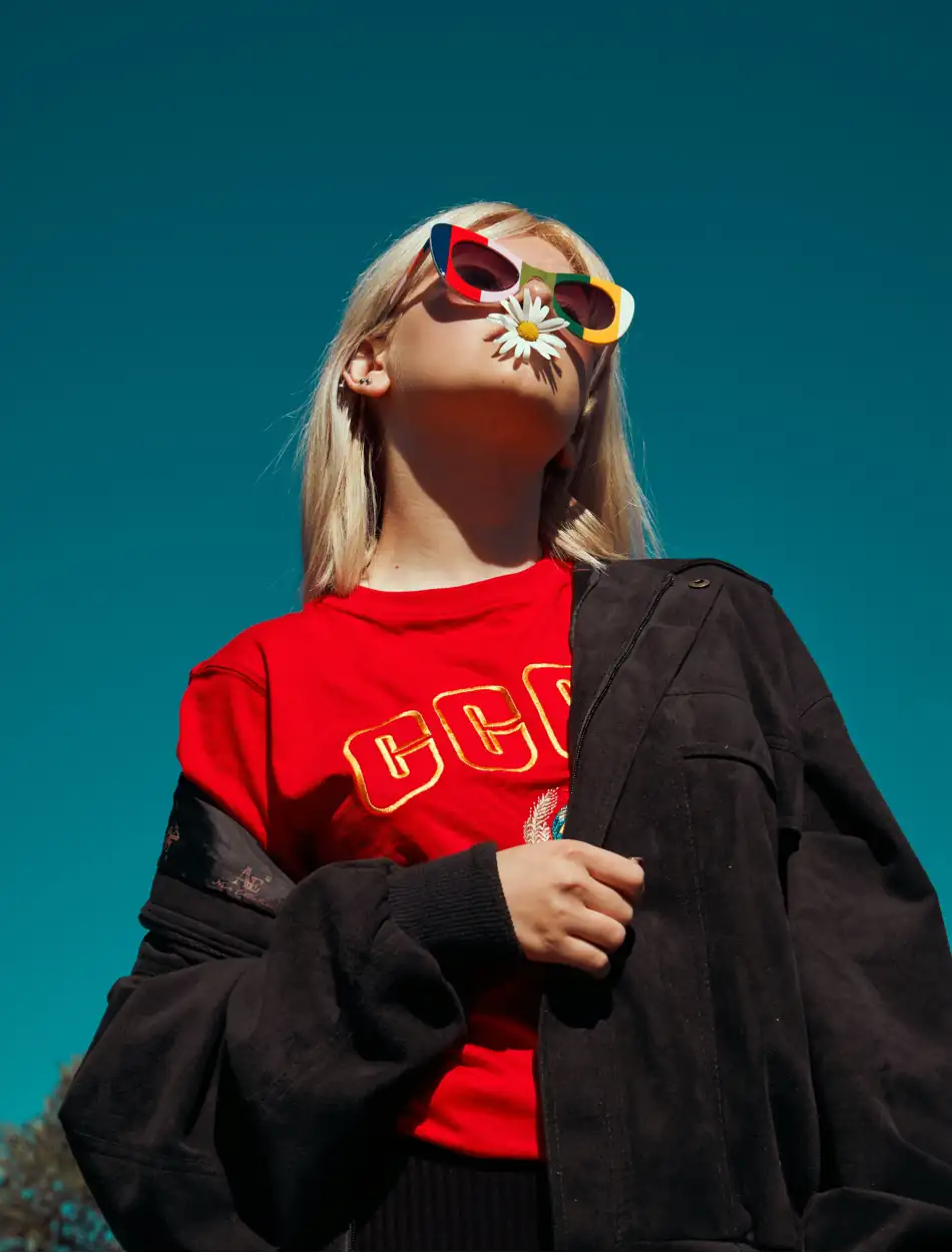 Editorial picture of a blond woman with retro sunglasses and a daisy in her mouth 